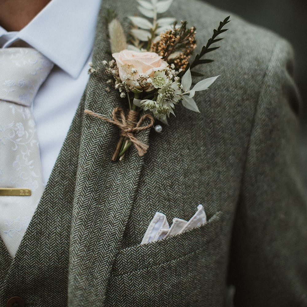 Groom wears pastel rose buttonhole tied with brown string 