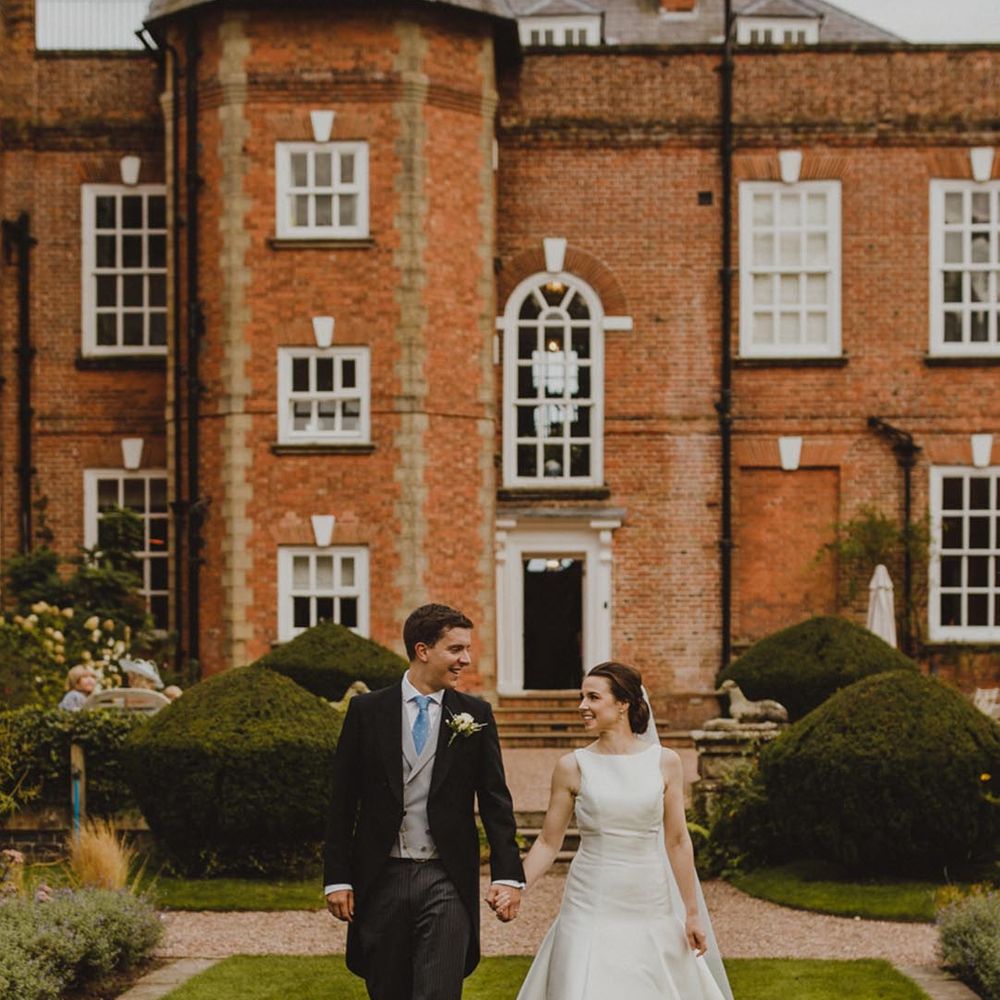 Bride in satin look sleeveless wedding dress and groom in dark suit walking round the grounds of Iscoyd Park