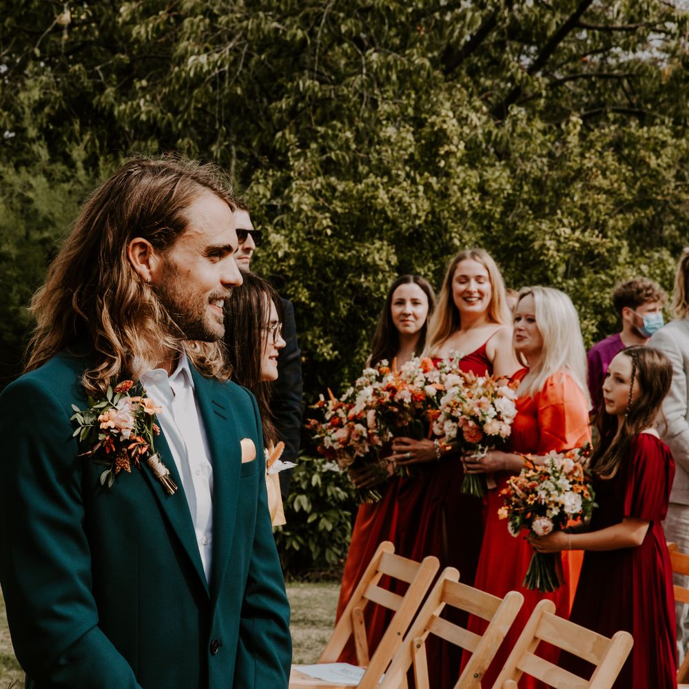 Groom wears green suit with colourful floral buttonhole 