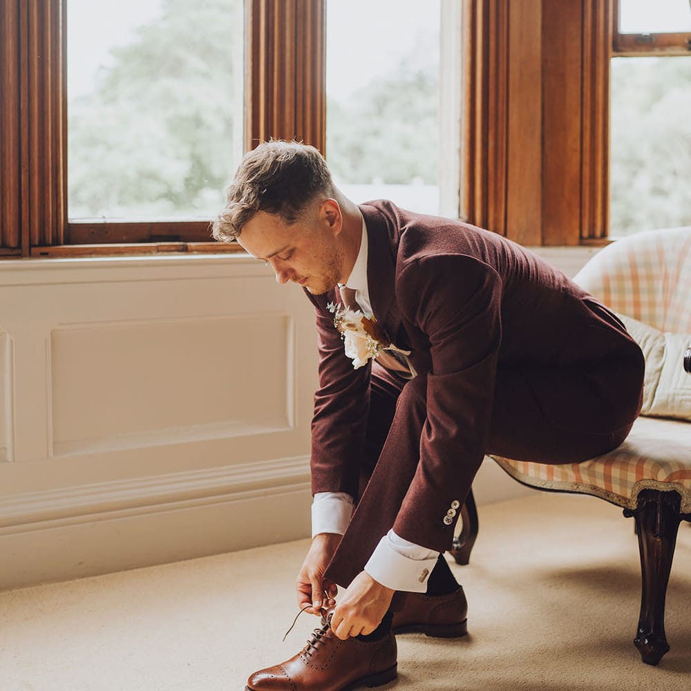 Groom wears maroon suit complete with brown brogues and floral buttonhole 