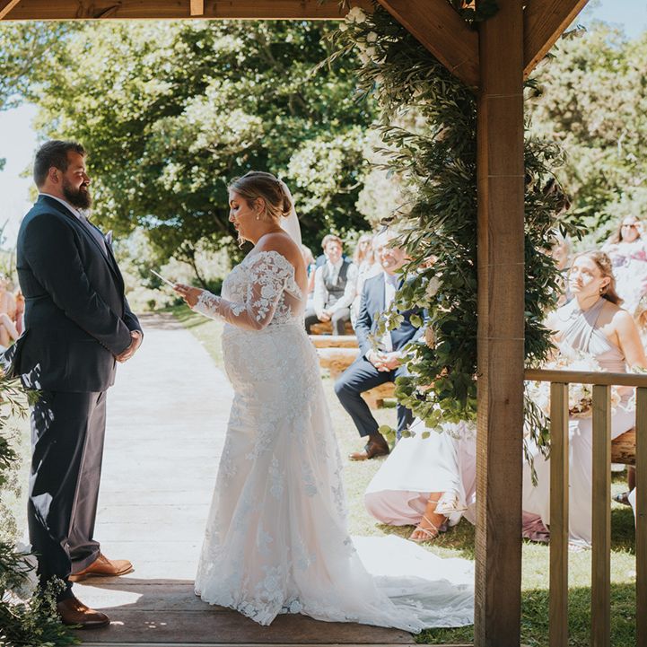 Bride & groom read wedding vows to one another beneath pergola outdoors for Watermouth Cove wedding 