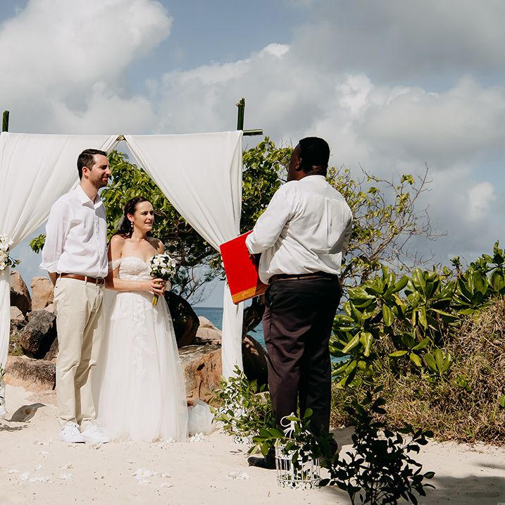 Bride and groom at Seychelles elopement on the beach with chiffon white wedding arch with white tropical flower decorations and bunches of tropical syzygium formosanum 
