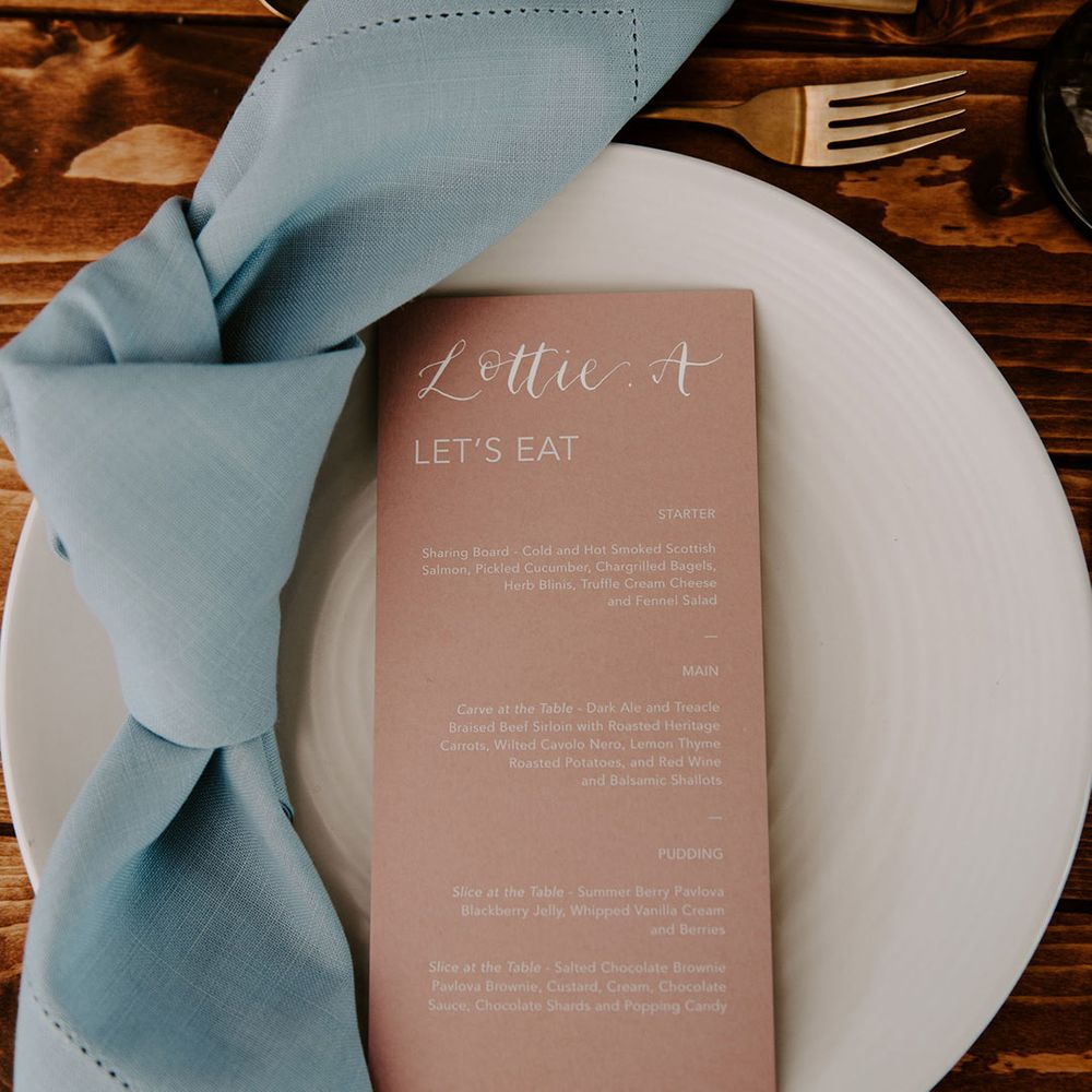 Pink wedding menu with blue napkin on white plate for pastel theme wedding reception with gold cutlery 