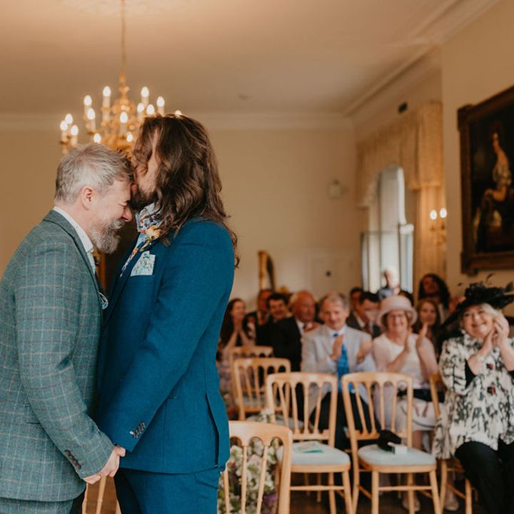 Groom with long hair kisses his groom on the forehead after wedding ceremony 