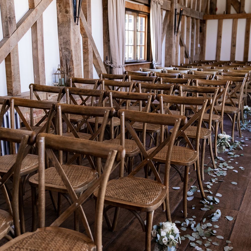 Rustic aisle decor at Gate Street Barn complete with wooden chairs and eucalyptus leaves lining the aisles alongside small white floral arrangements