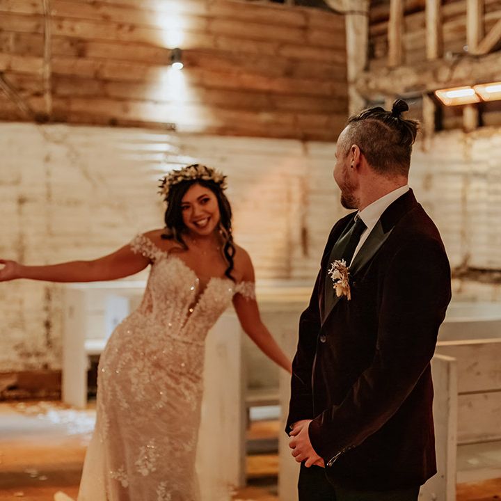 The groom in a burgundy velvet suit jacket turns around and sees the bride for the first time wearing a sparkly lace wedding dress 