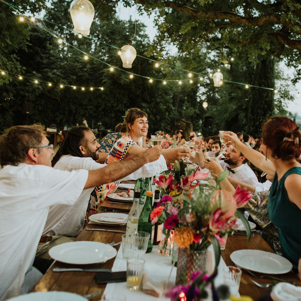 Guests at outdoor wedding in Italy cheers with champagne glasses surrounded by fairylights and pink flower decor