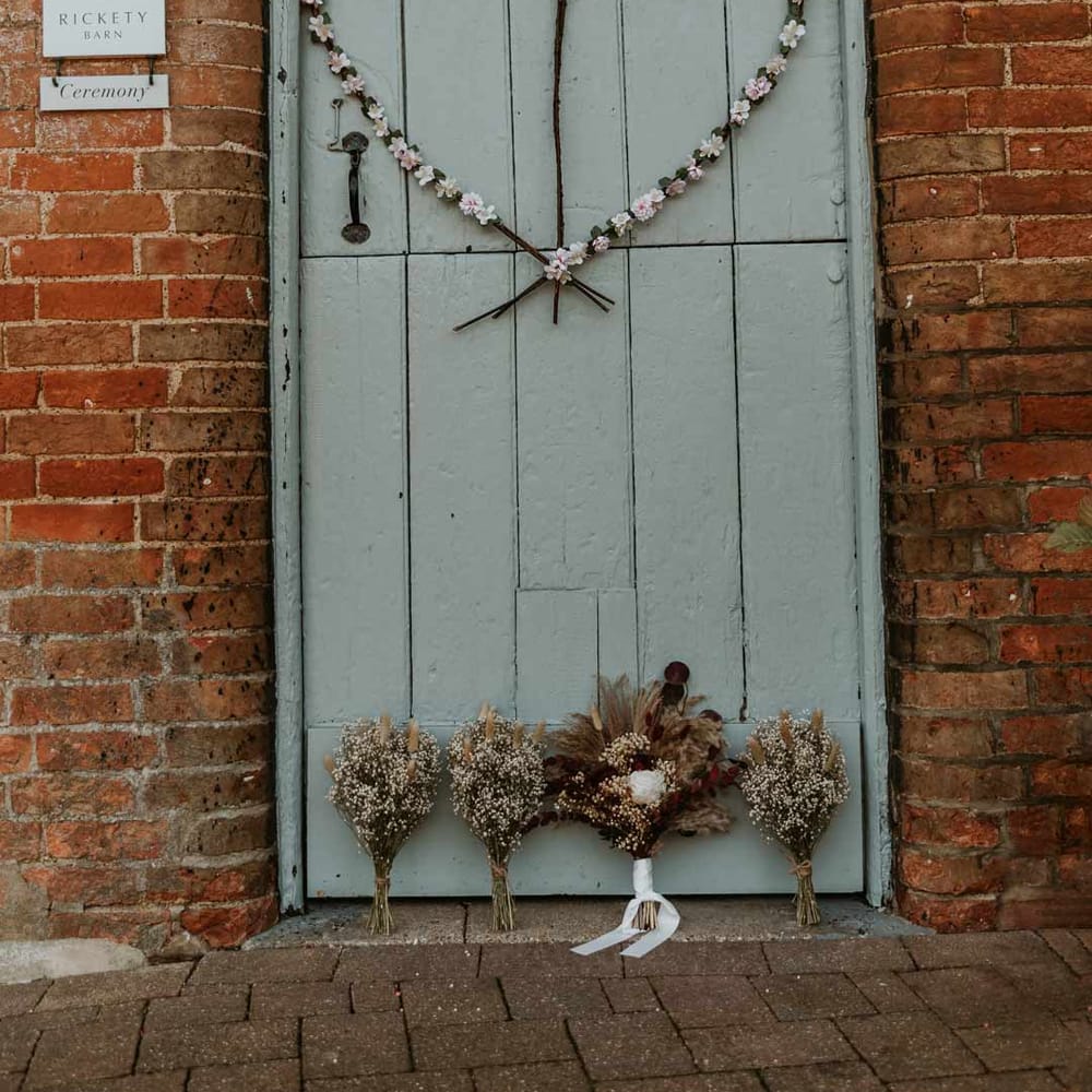 Baby blue barn door with heart shaped wedding wreath and autumnal boho dried flower bouquets at Bassmead Manor Barns