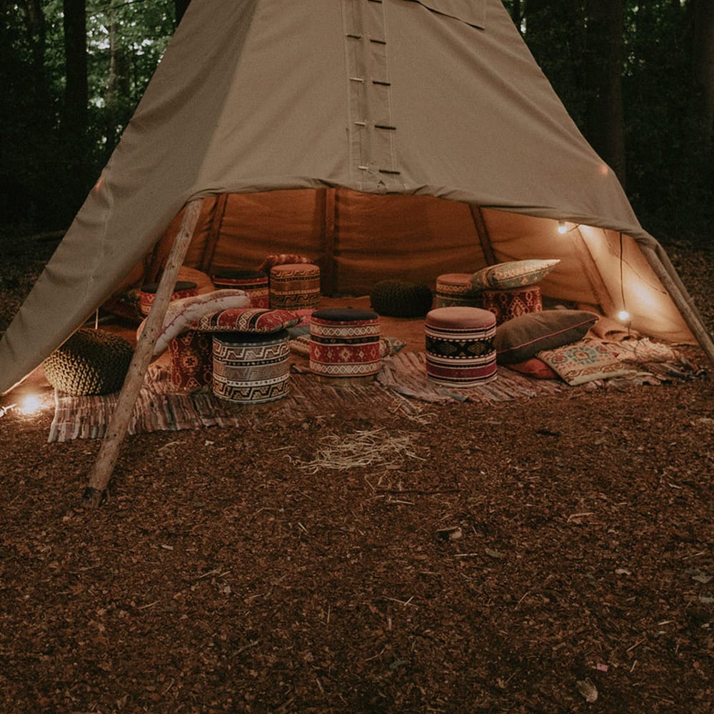 Cosy outdoor tipi area with stools, cushions, and throw blankets at boho wedding 