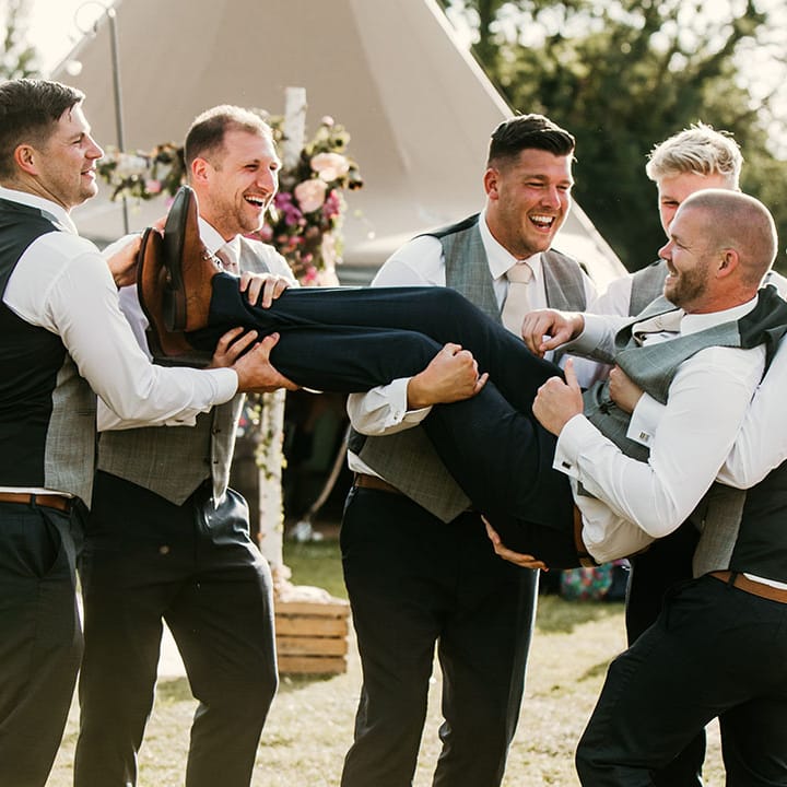 Groomsmen lift the groom up and pose for funny wedding photo 