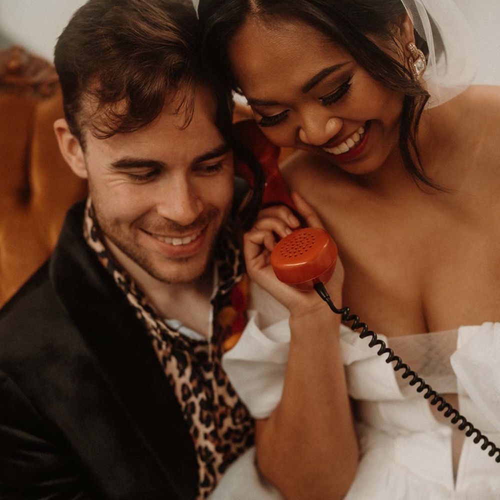 Bride in off shoulder tulle short wedding dress and groom in wet look black grooms suit with leopard print shirt doing wedding audio guest book 