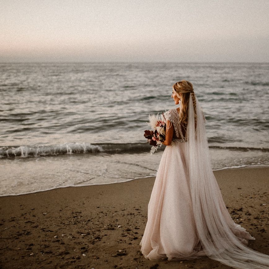 Bride on the beach with her bouquet and long cathedral length veil