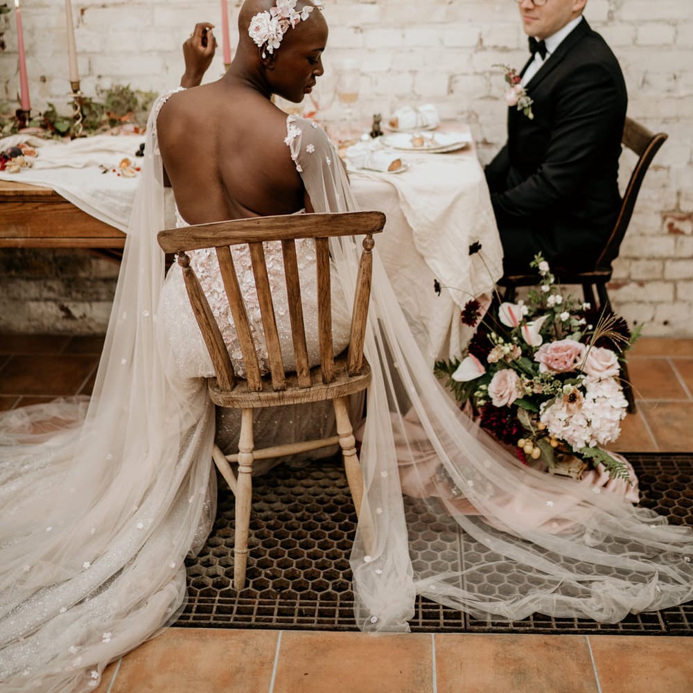 Bride with alopecia sitting at her wedding breakfast in a backless wedding dress with watteau train 