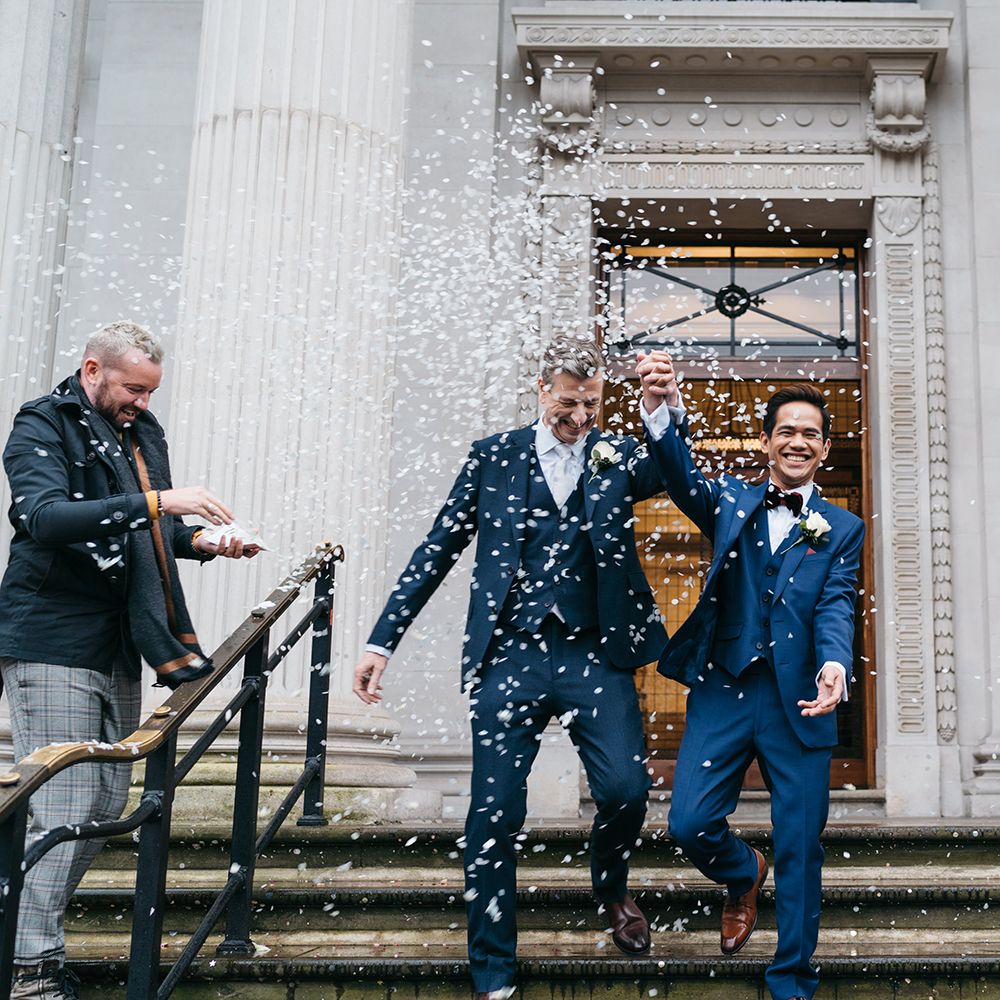 Grooms leave Old Marylebone Town Hall with blue confetti being thrown around them