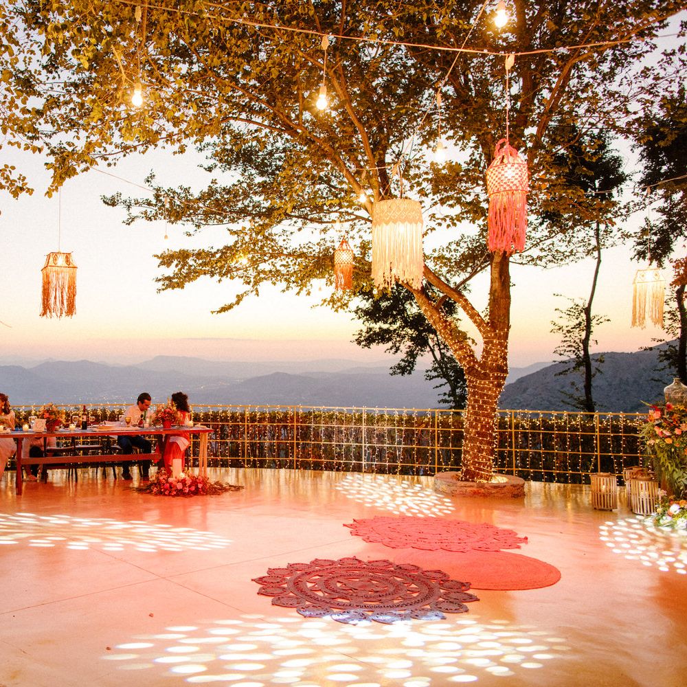 String lights covering the trees and railings, lanterns in the trees and guests sitting at the table as the sun begins to set