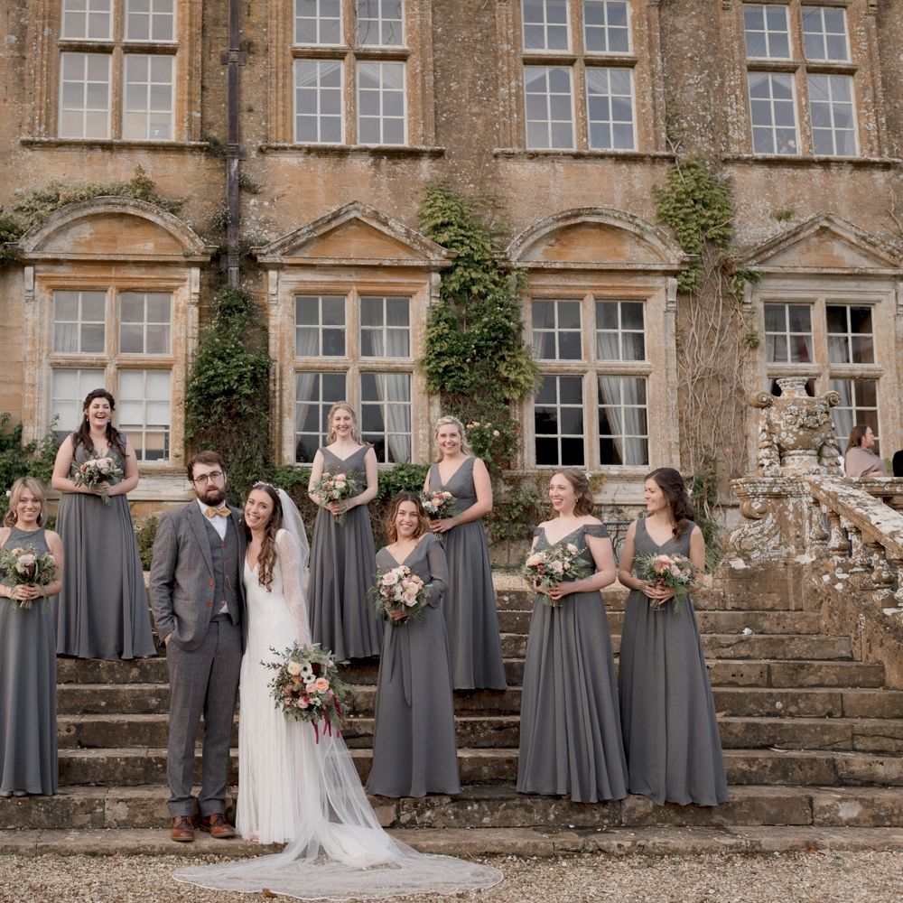 Bride and groom wedding day photography with bridesmaids wearing dark grey bridesmaid dresses outside Brympton House