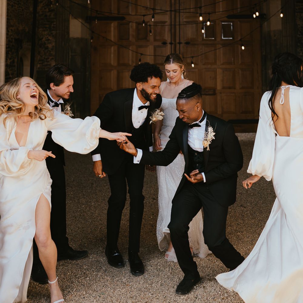 Wedding party portrait with bridesmaids and groomsmen in horseshoe waistcoats laughing 