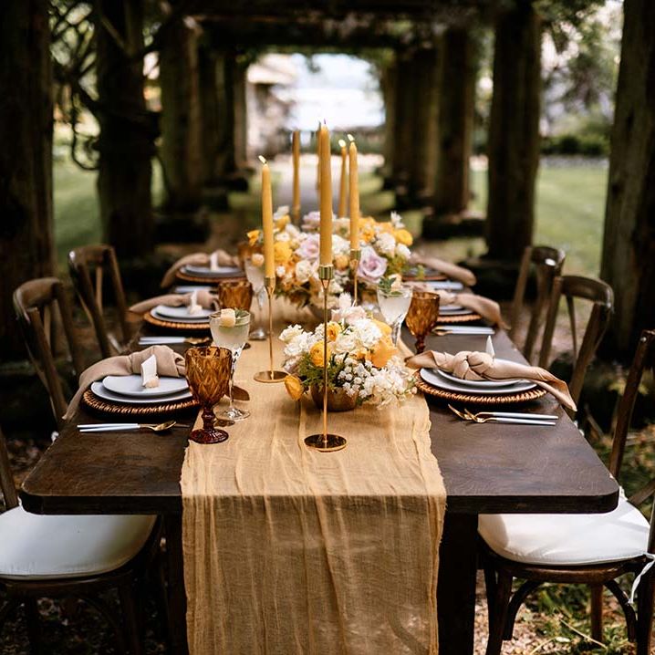 Alfresco wedding reception table decor with wooden table, yellow table runner and gold candlesticks 