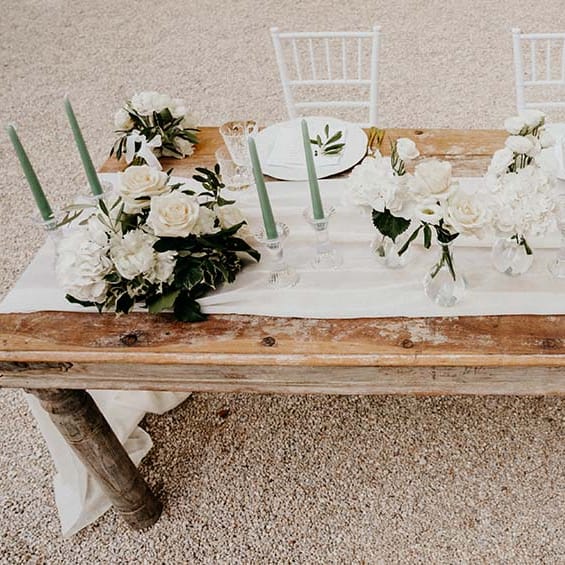 Rustic tablescape complete with green foliage and white florals and green candlesticks  | Royal Studio