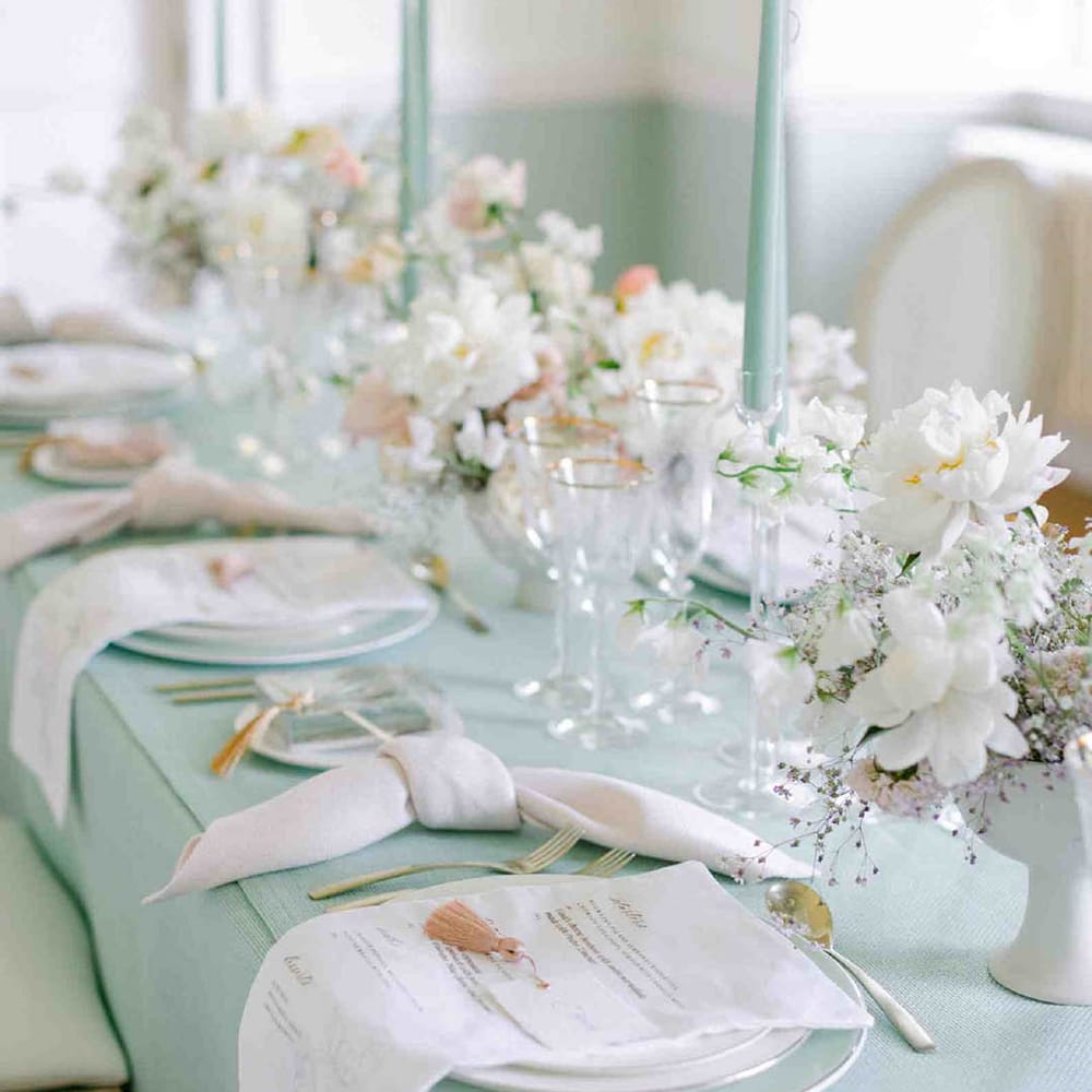 pastel tablescape decor with pale green tablecloth and taper candles and white tableware 