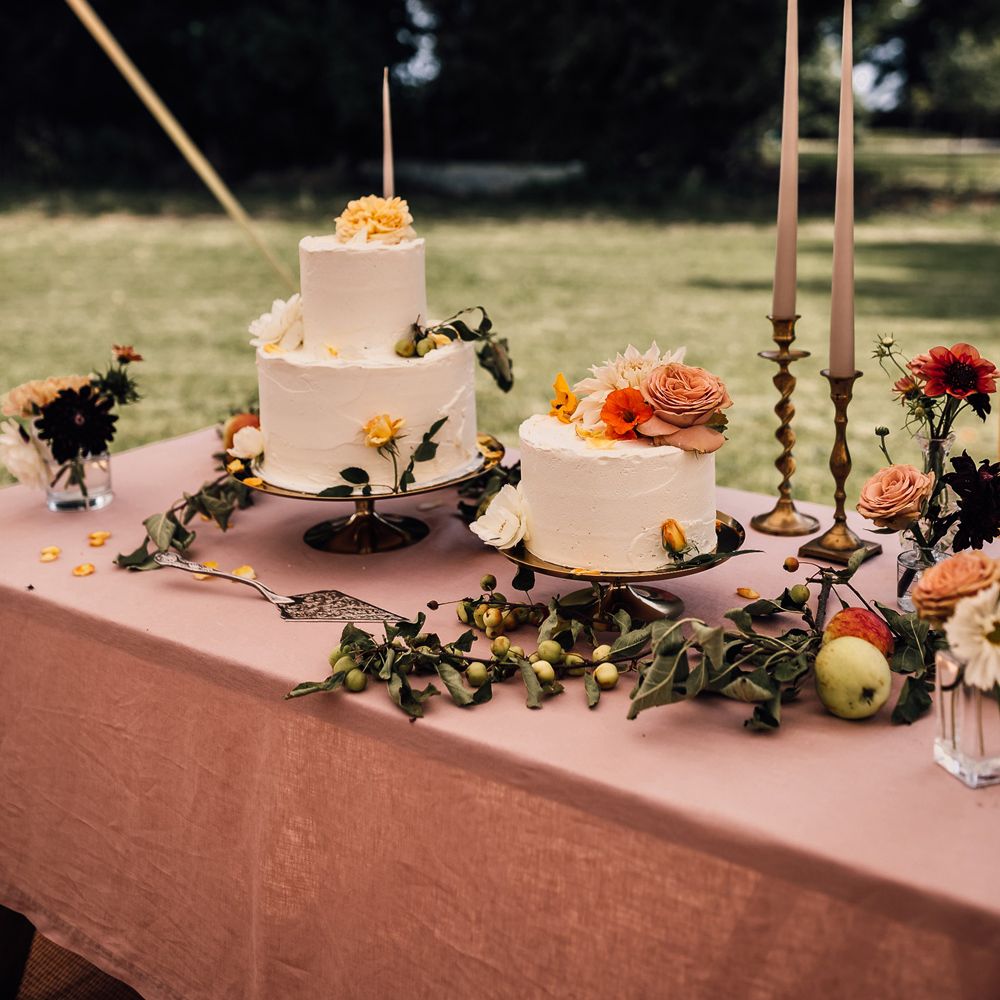Dusky pink wedding table with white cake wedding cakes with floral decor, pink dinner candles and assorted foliage for marquee wedding reception in Cornwall