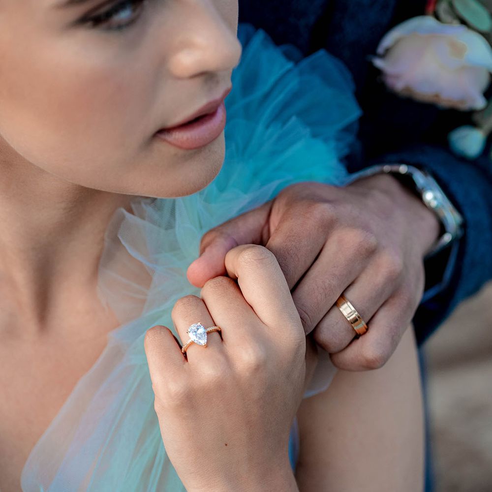 Groom with a gold wedding band and bride with a rose gold pear shape diamond engagement ring holding hands 