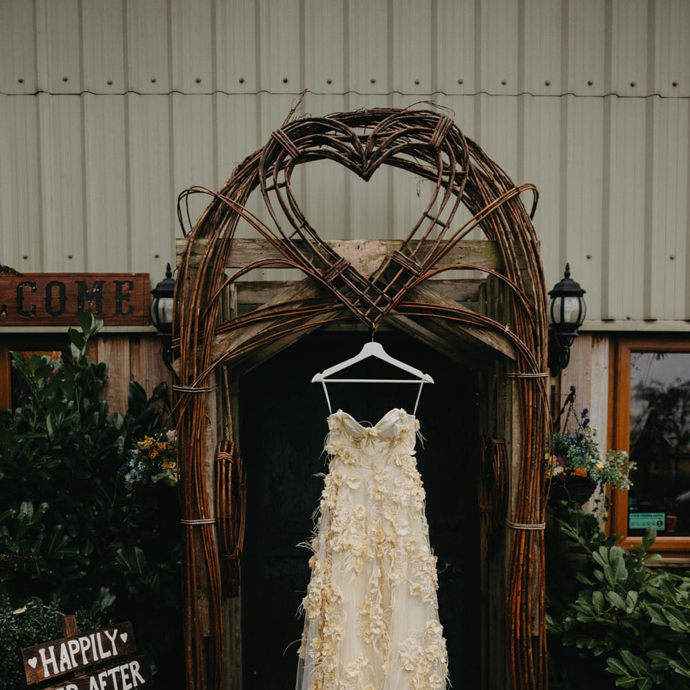 Applique feather wedding dress with cami straps and tulle hanging in doorway at rustic farm wedding