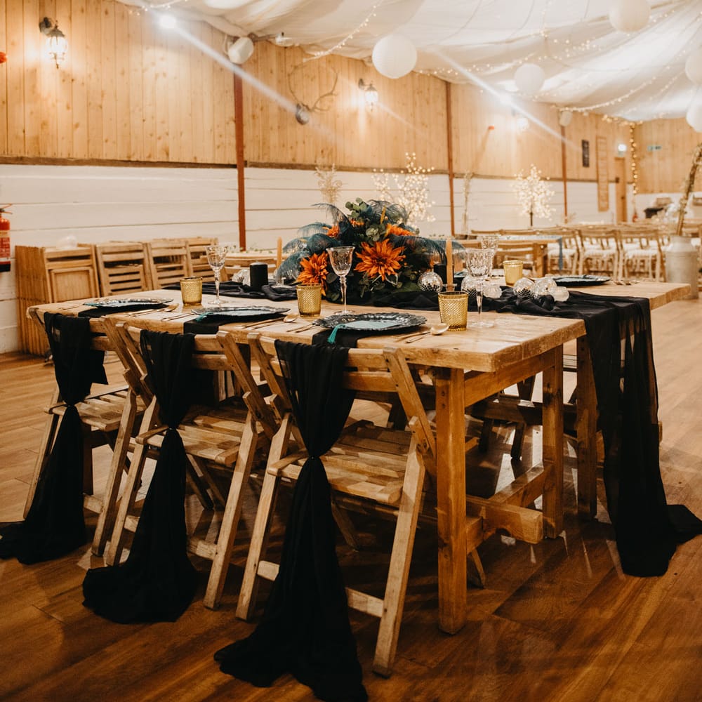 Rustic wedding reception with wooden tables, chairs and fairy lights and blue and orange florals for Wellbeing Farm wedding in Lancashire