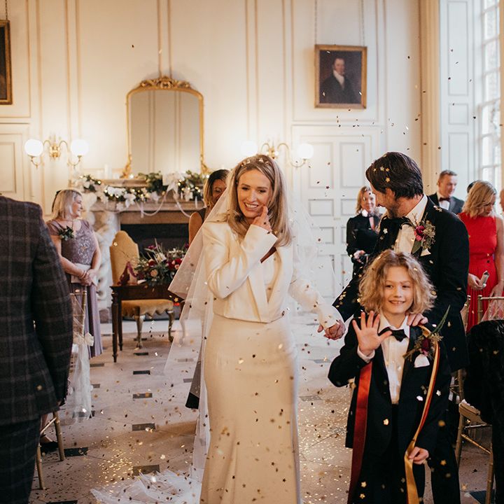 Bride walks down the aisle wearing Nefertiti Crown, Suzanne Neville bridal gown and Zara padded bridal jacket 