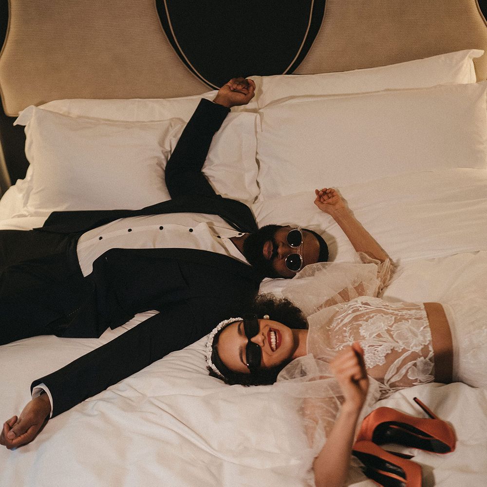 Black bride and groom laying down on the bed at Mayfair Townhouse hotel in sunglasses 