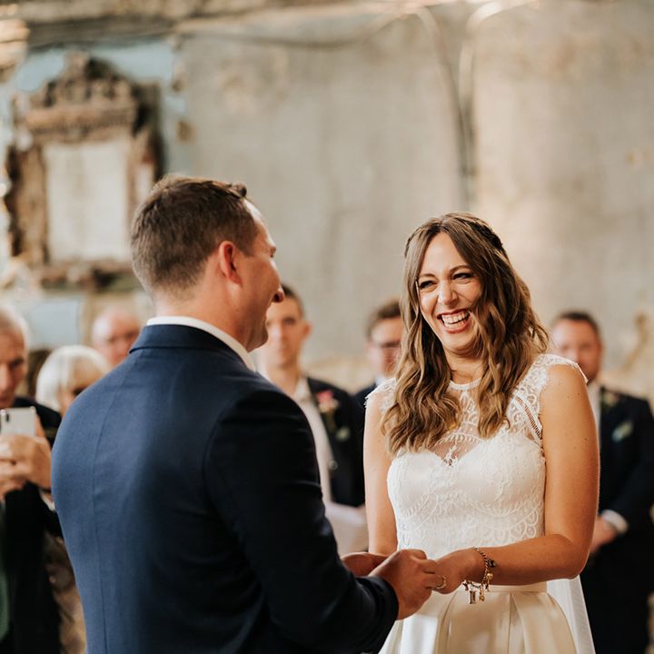 Bride and groom smile at each other at the altar of their wedding as groom slides wedding ring onto bride's finger