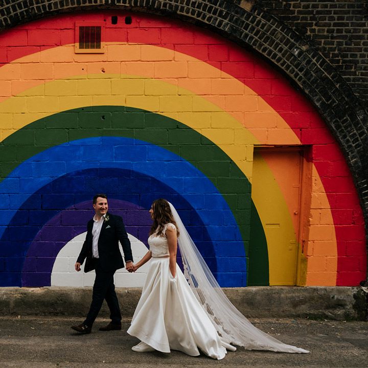 Bride and groom walk in front of rainbow painted backdrop at 100 Barrington venue in Brixton, London