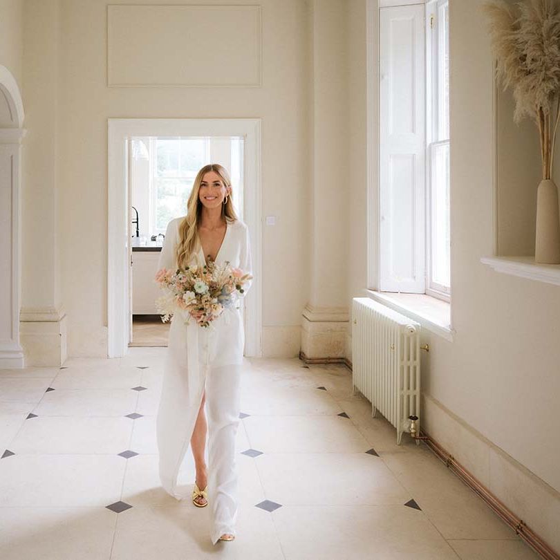 Bride walks in her custom Bon Bride wedding dress with long sleeves and a belt with pastel bouquet