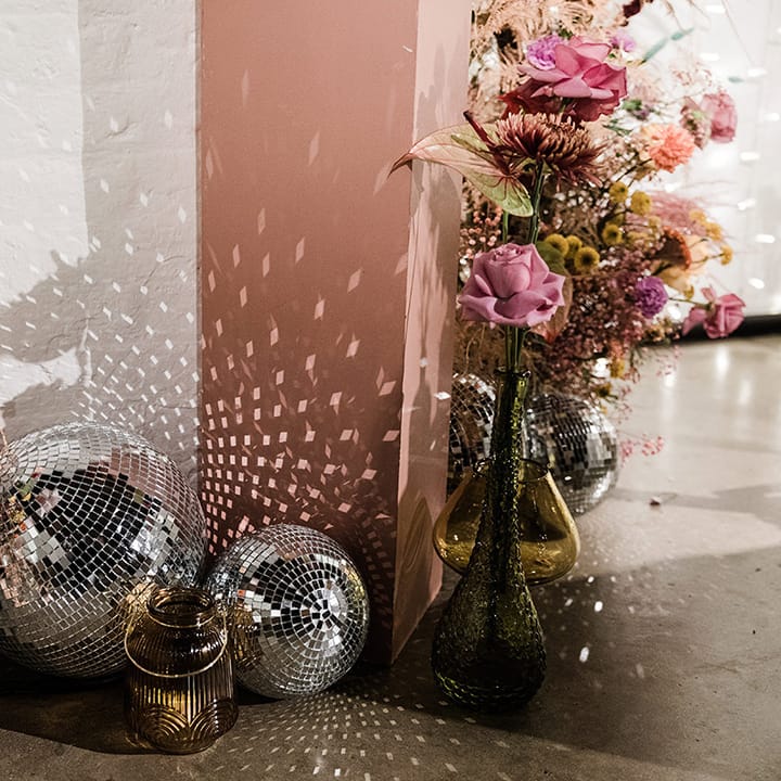Coloured glassware vases with bright flowers and disco ball decor for 60s inspired wedding