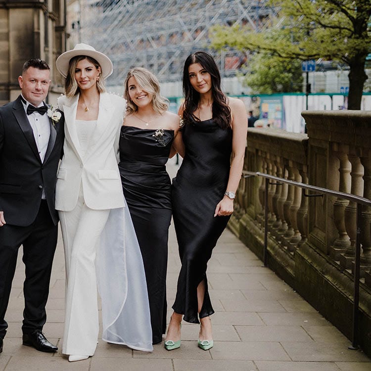 Bride in Nadine Merabi pearl trouser suit with bridal party in black tie and black satin bridesmaid dresses 