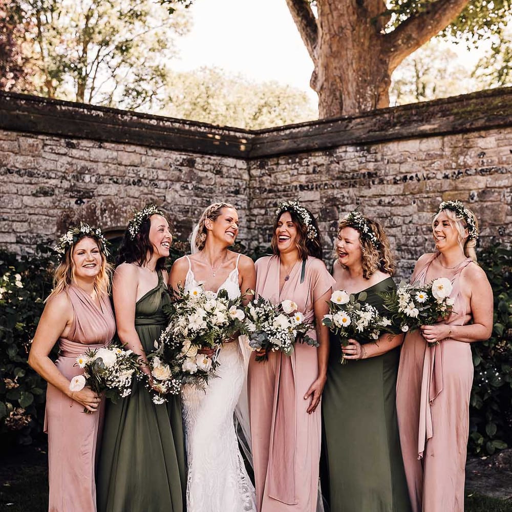Bride with braided updo with bridesmaids in pink and green dresses with white flower bouquets 