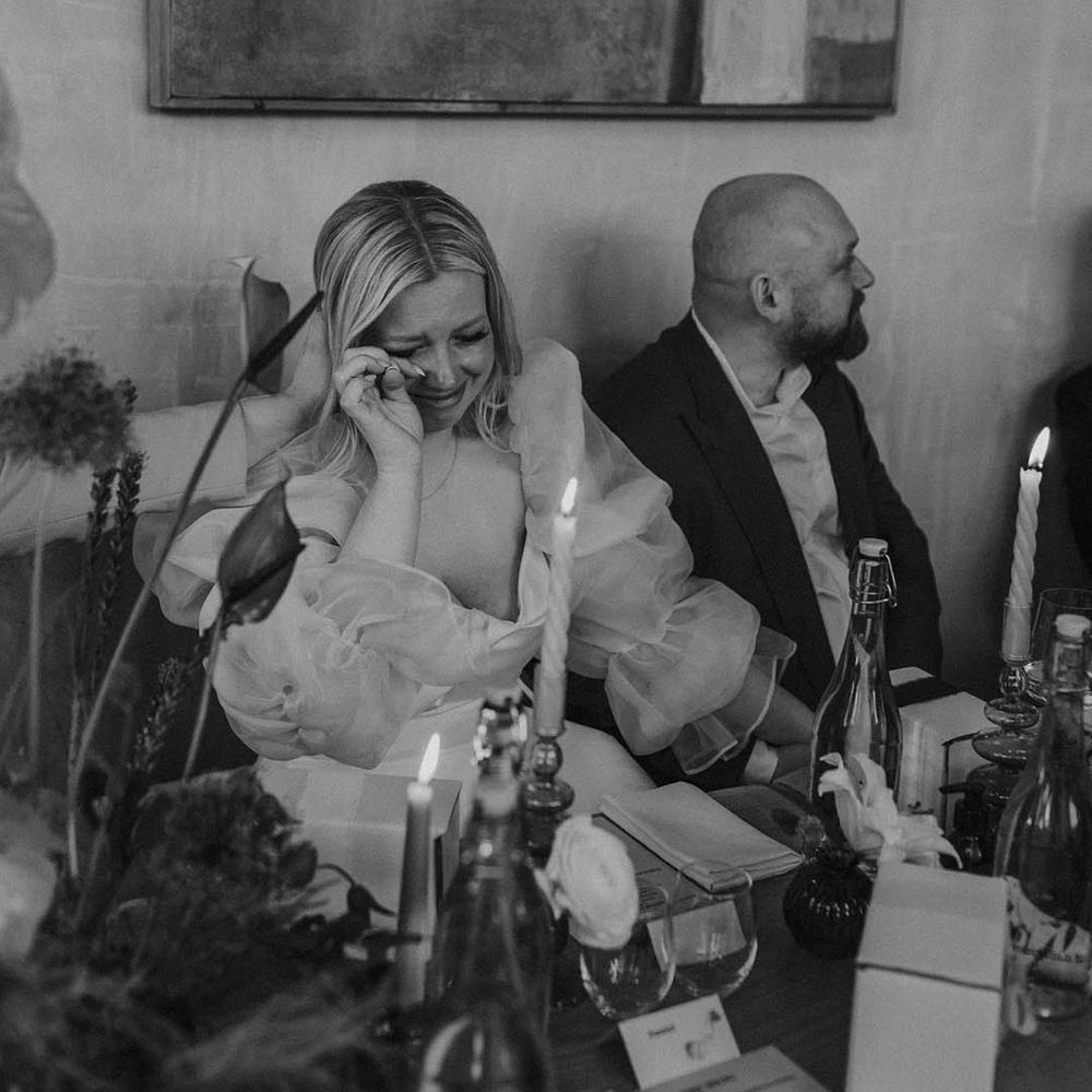 candle lit wedding reception with emotional bride in long sheer sleeve wedding dress wiping her tears 