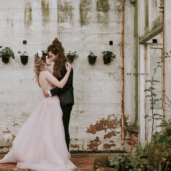 Bride in a pink wedding dress and groom a black suit embracing in the conservatory at Hooton Pagnell 