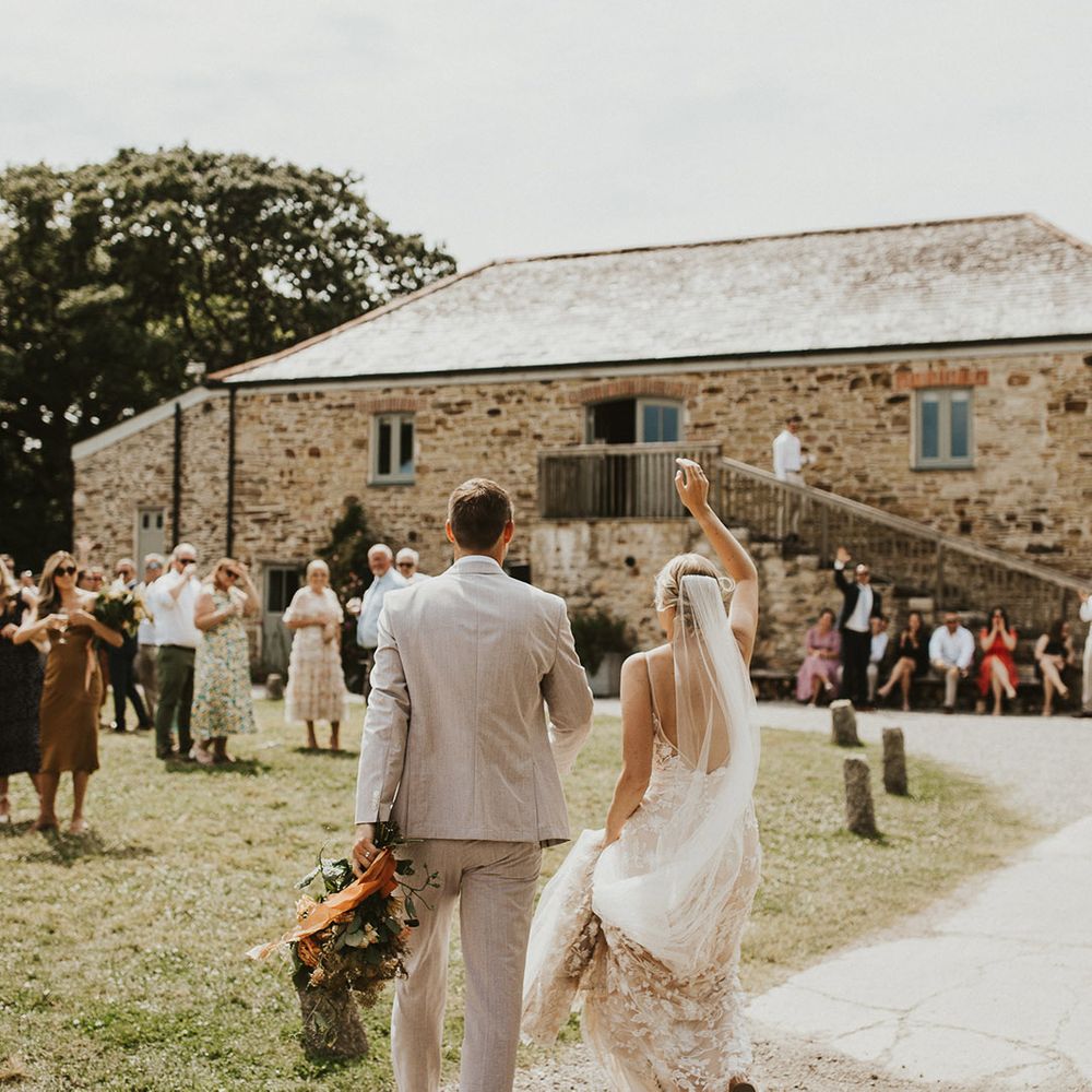 Bride and groom lift up their hands as they enter their outdoor wedding reception 