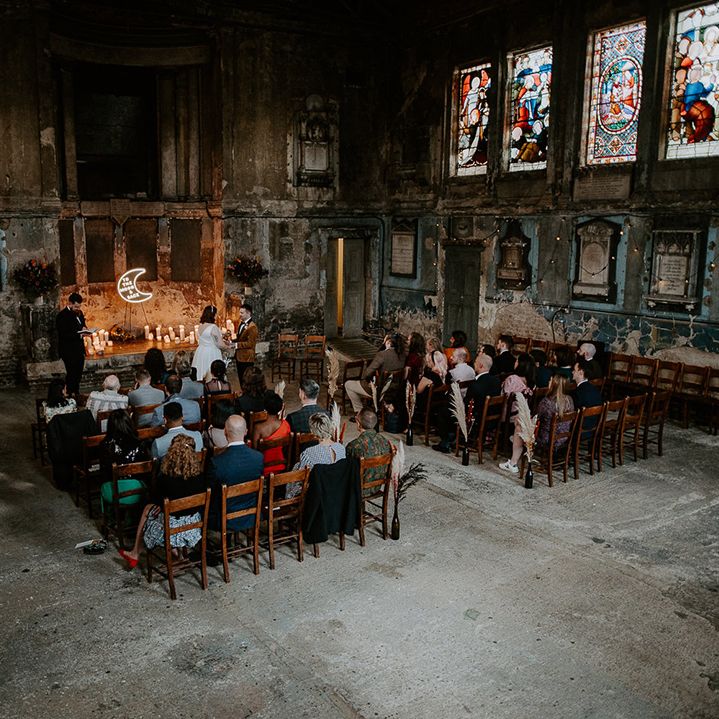 The wedding ceremony taking place at industrial venue in London featuring a moon neon sign at the centre of the aisle