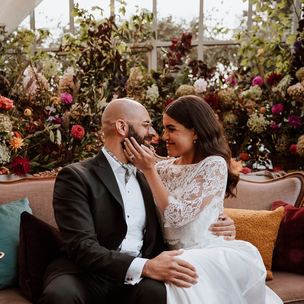 Bride in three quarter length sleeve wedding dress with lace detailing and full satin skirt and bottle green satin wedding shoes and groom in classic black tuxedo with hand painted silk cravat and handkerchief embracing each other 