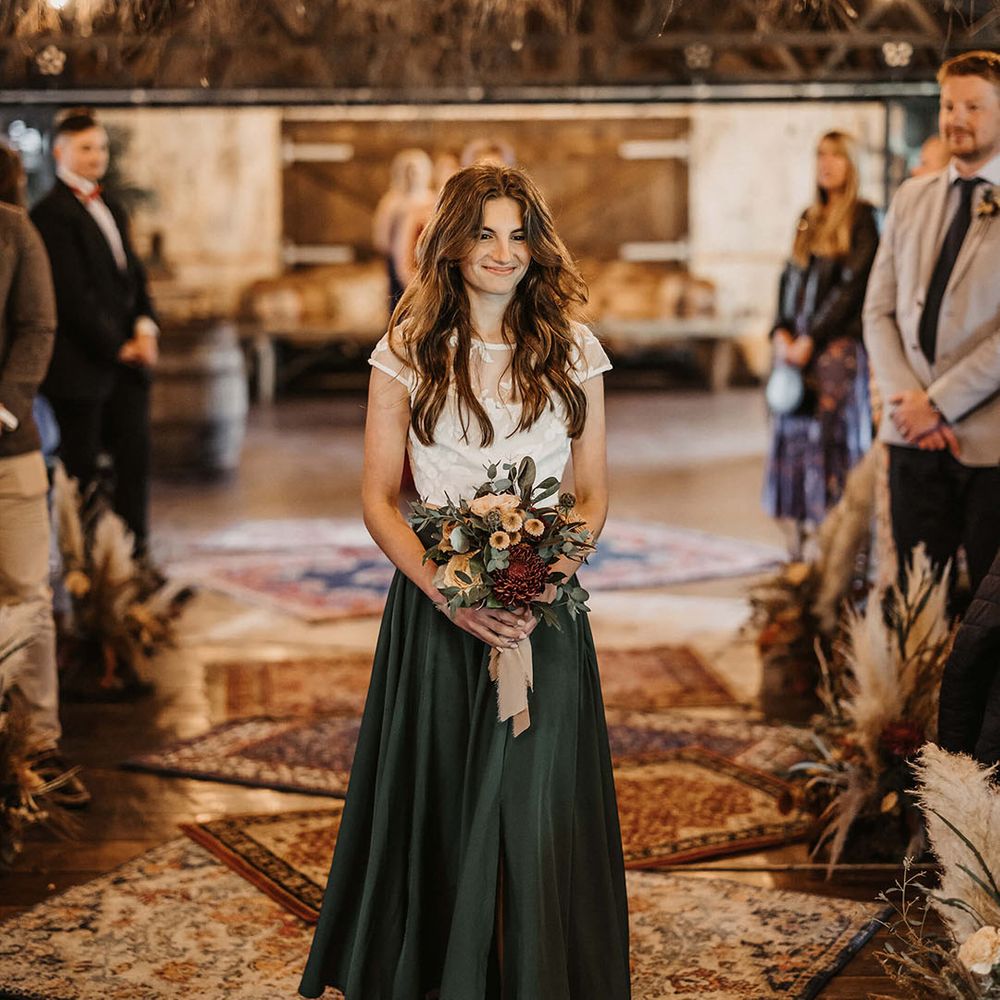 Bridesmaid in green silk skirt and white top walks down the aisle 