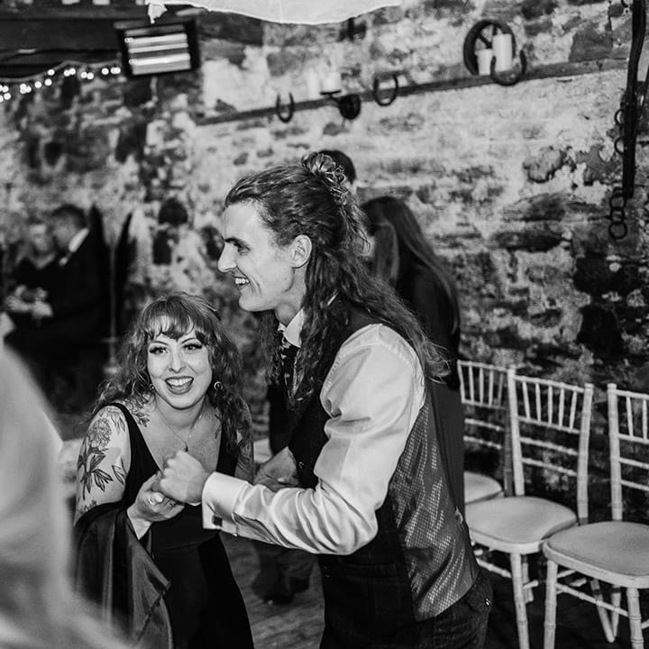 Bride in v neck black wedding dress and groom in alternative groom suit dancing to live wedding band at boho themed wedding 