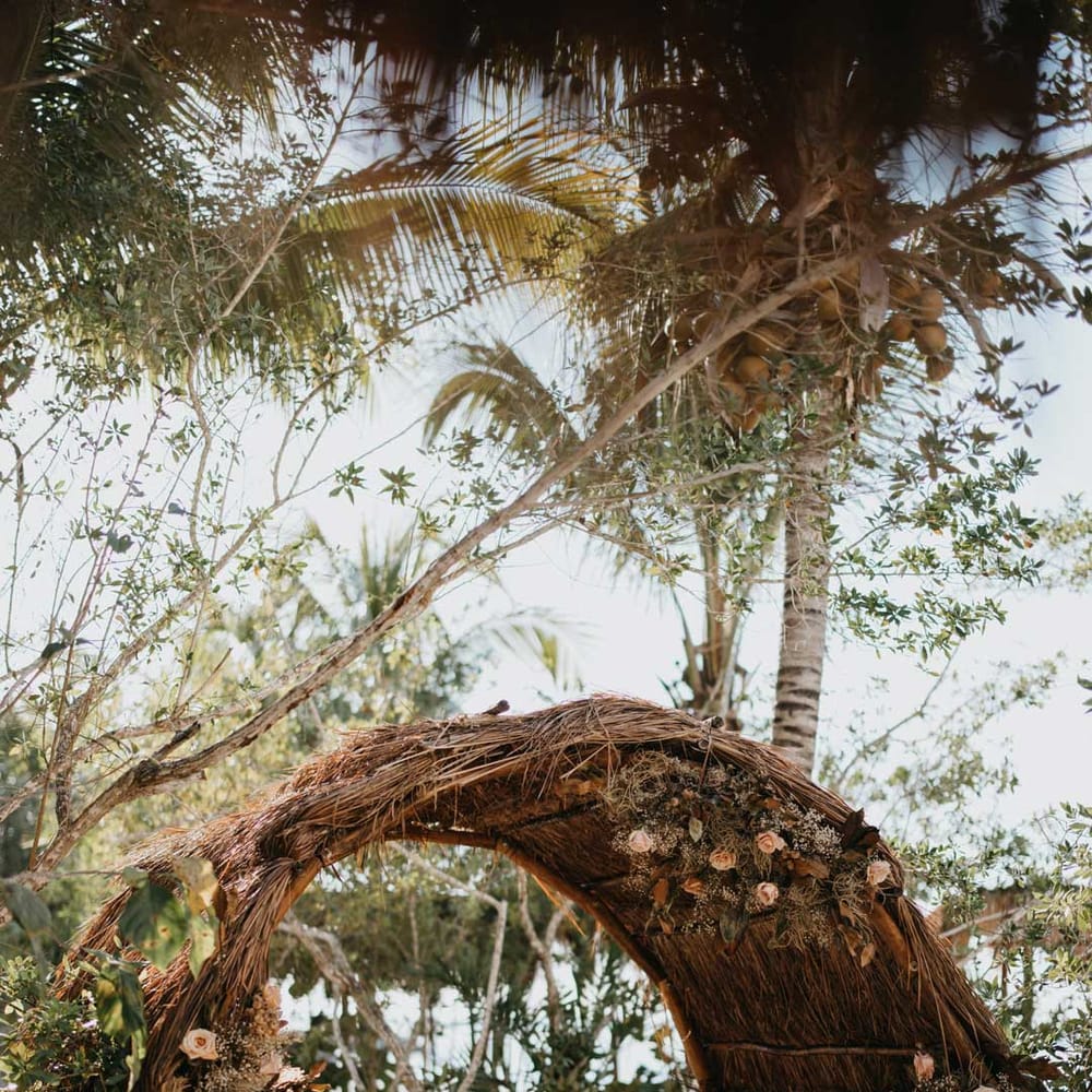 Large bamboo wedding arch on beach at destination wedding in Mexico with dried garden flower and foliage flower arrangements 