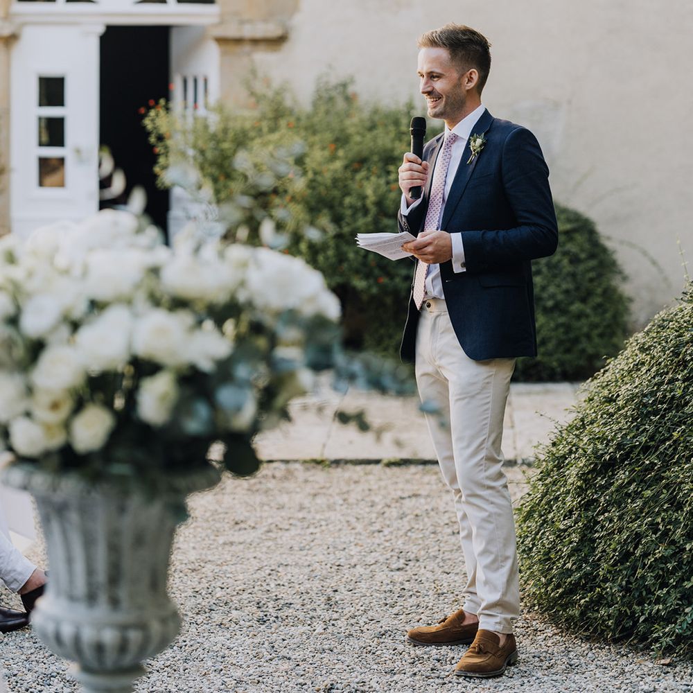 Groomsman in stone chinos and a navy blazer giving a wedding speech during the al fresco reception 