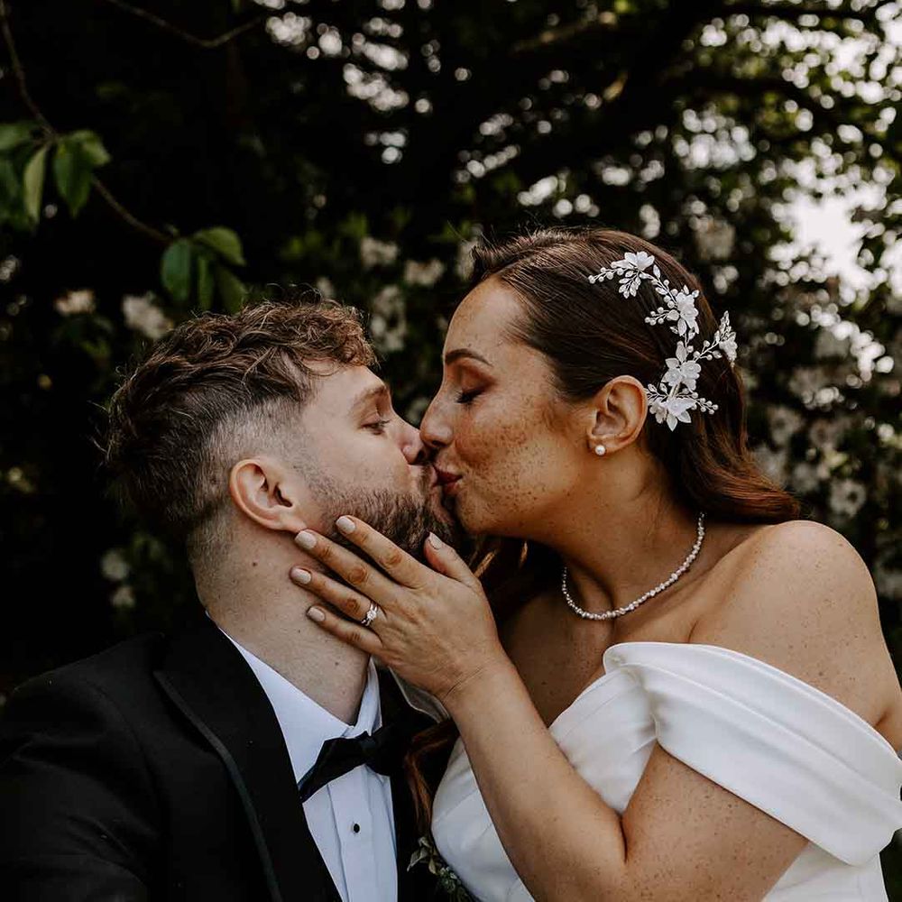 bride with flower hair accessor kissing her groom in a tuxedo