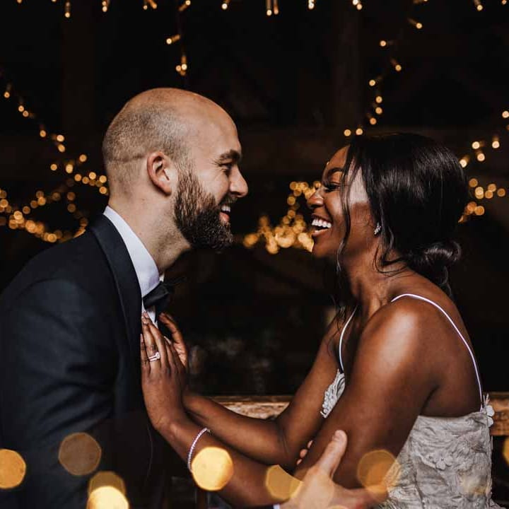 Bride and groom embracing and laughing surrounded by wedding fairy lights and festoon chandeliers in Lains Barn reception room
