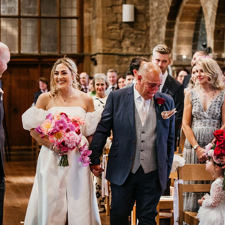 Father of the bride holds back his tears as he walks the bride down the aisle to meet the groom 