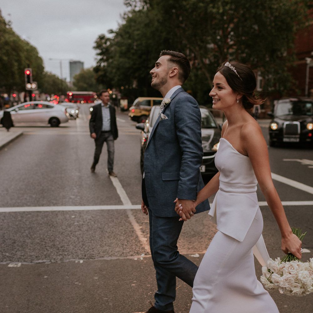 Stylish bride in strapless Roland Mouret wedding dress and groom in blue suit walking through London