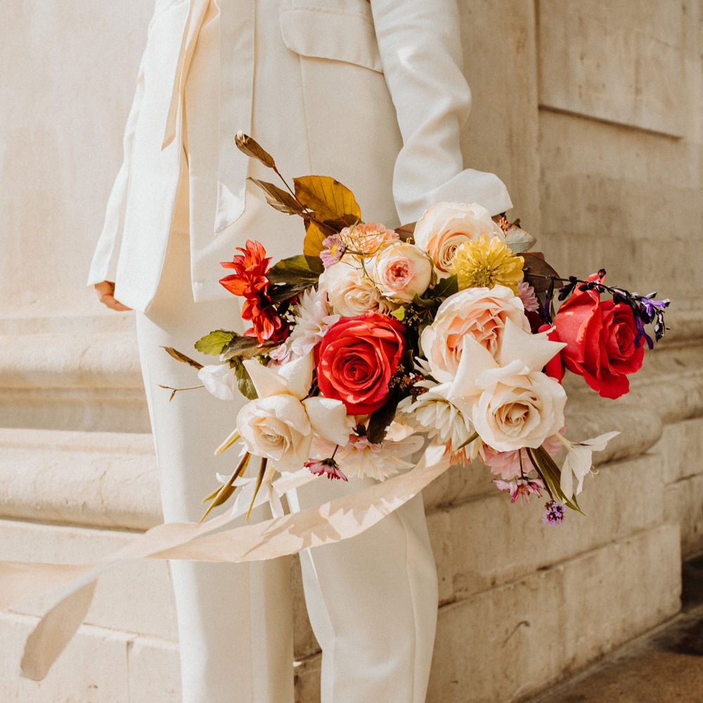Bride in a trouser suit holding a brightly coloured wedding bouquet 